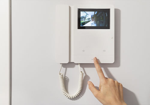 Una persona señala un timbre con vídeo en una pared blanca.